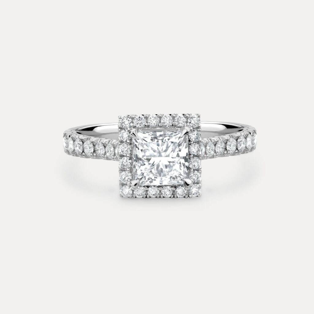 Princess cut diamond surrounded by a halo of round brilliant diamonds. Set in a platinum band with diamond set shoulders.